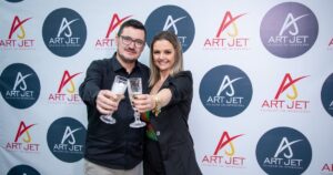 Equipe da Art Jet brindando em frente ao painel da empresa, simbolizando confiança e qualidade nos serviços de impressão profissional para empresas.