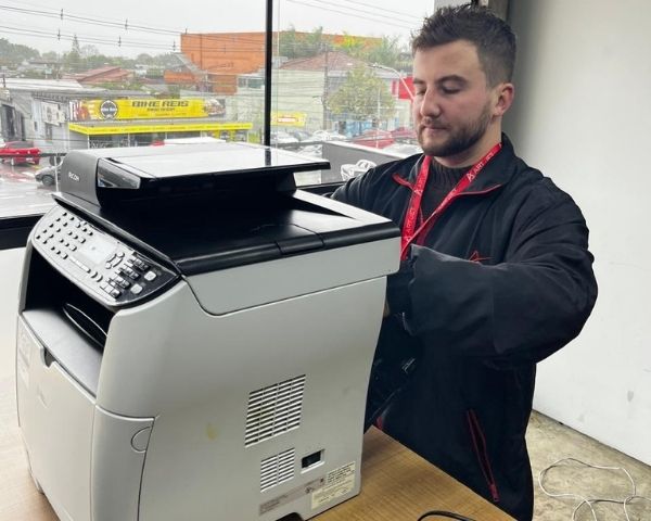 Técnico da Art Jet realizando manutenção em impressora empresarial durante atendimento a uma pequena empresa.