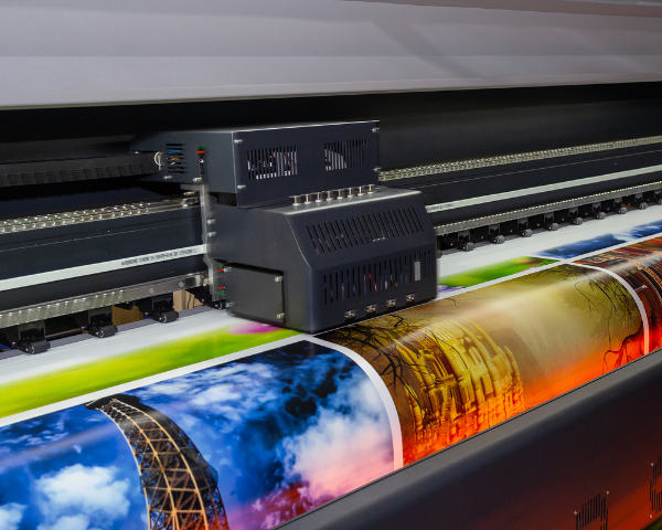 Impressora de grande formato produzindo material gráfico com sangria para acabamento.