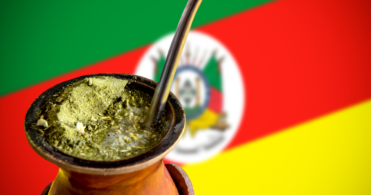 Cuia de chimarrão com bandeira do Rio Grande do Sul ao fundo para Semana Farroupilha